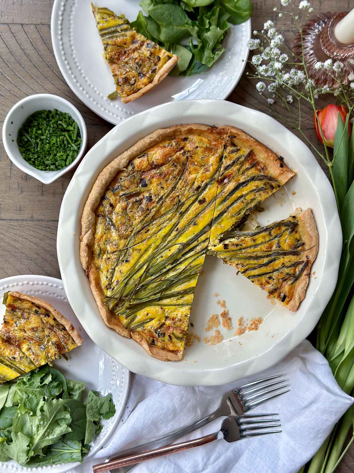 Spring vegetable quiche served two slices on each plate with side salad and fresh chives and forks nearby.