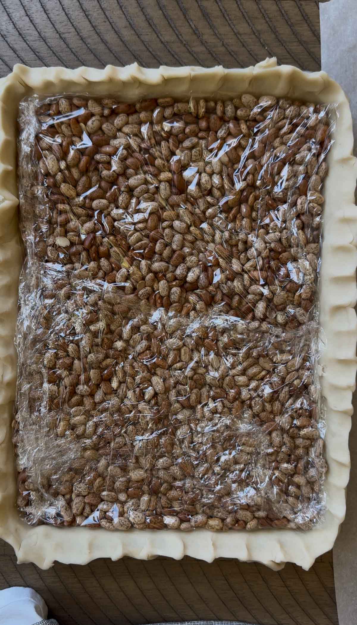 Prepped pie crust in a pan covered with cling wrap and weighed down with pie weights.