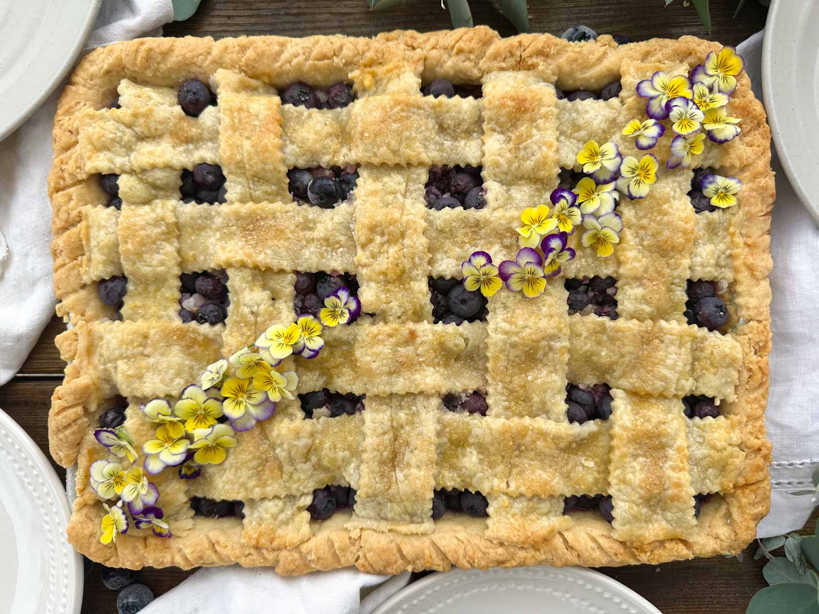 Blueberry Slab Pie with golden brown lattice pie crust, with mini pansy flowers trailing across the pie amost meeting in the center.
