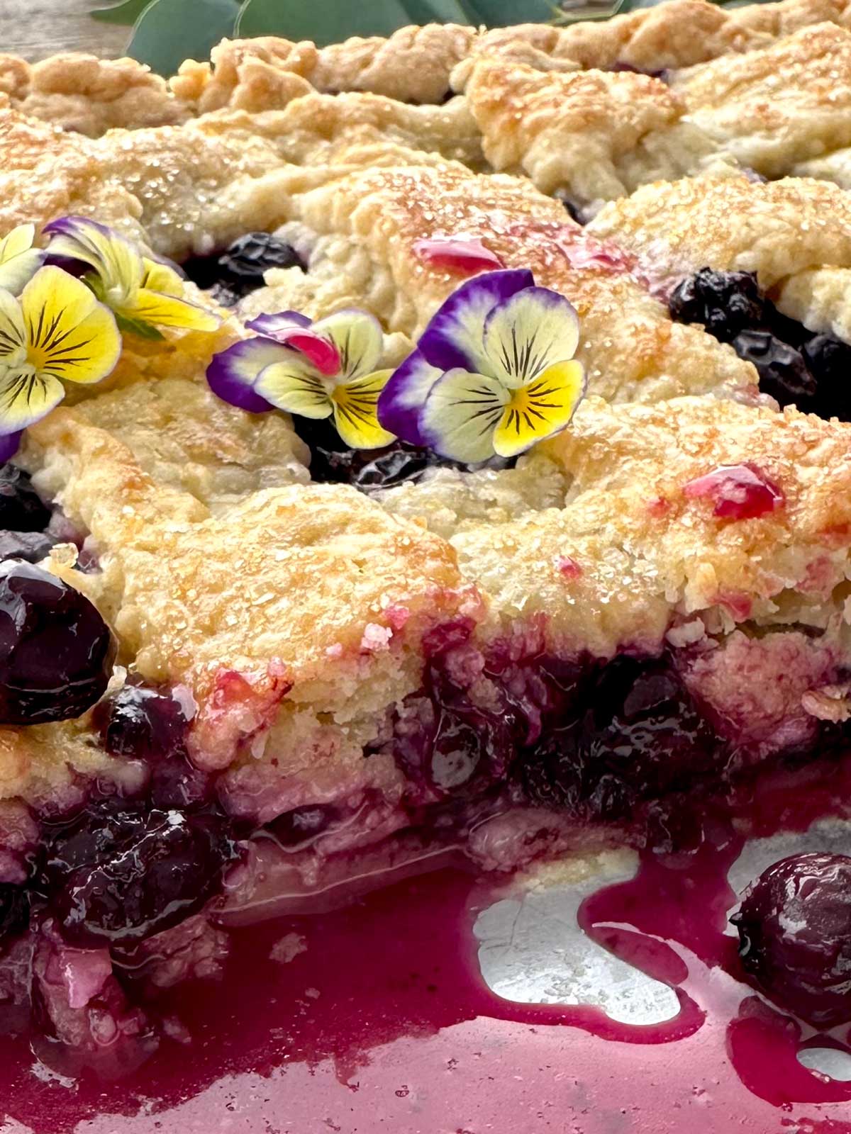 Close-up of sliced blueberry slab pie in a sheet pan with juices oozing between the cuts.