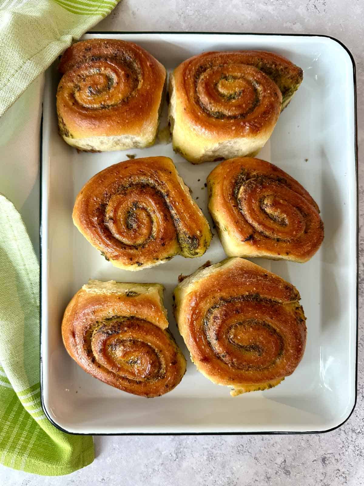 Six Pesto Pinwheel Pull Apart Bread on a white tray with a dish towel next to them.