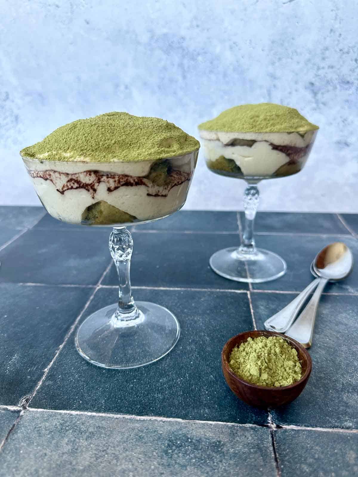 Match Tea-ramisu in two coupes with a small bowl of match powder next to it and two spoons.