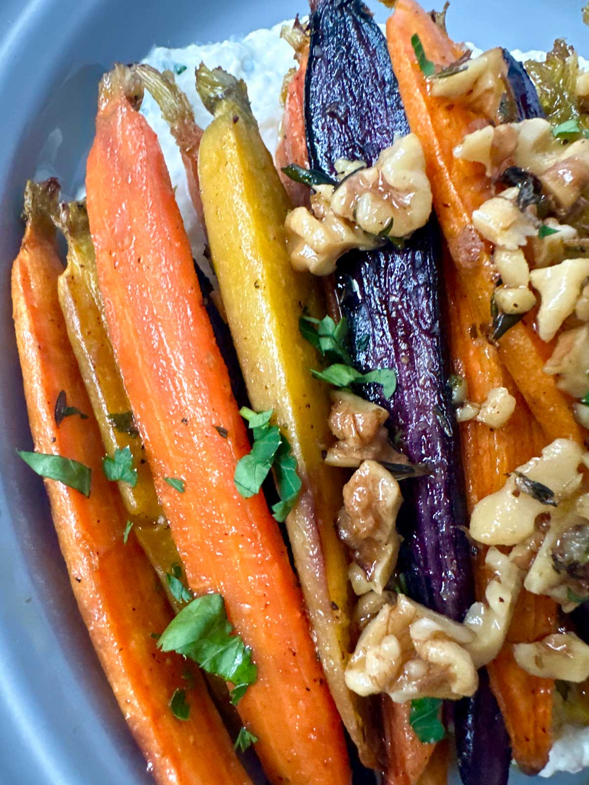 Close up of tri-colored carrots topped with walnuts and parsley.