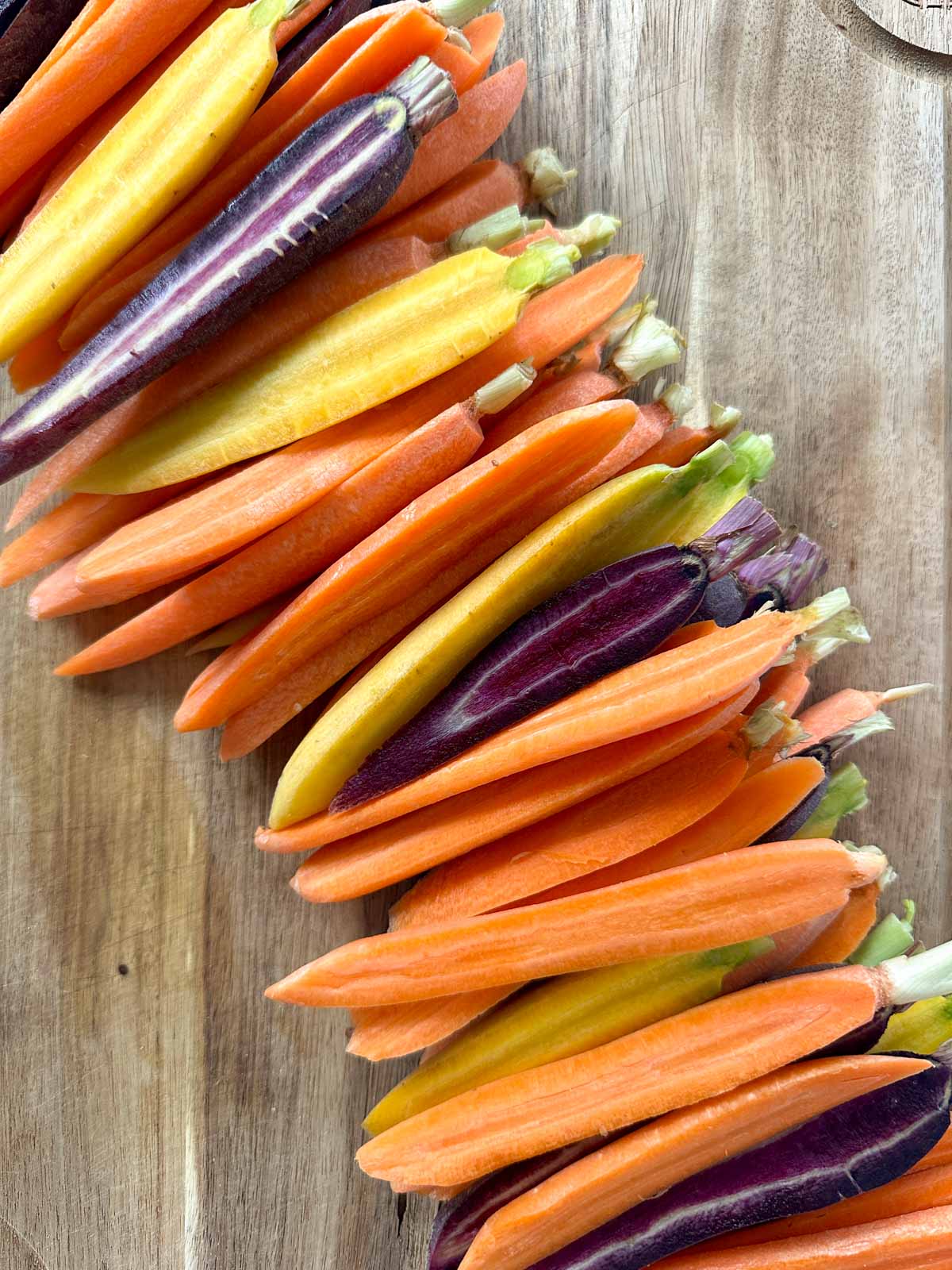 Yellow, orange, and purple carrots peeled and halved arranged on a cutting board.