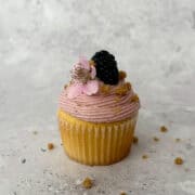 Blackberry Crumble Cupcake with Blackberry Cream Cheese Frosting and garnished with a whole blackberry and blackberry flower.