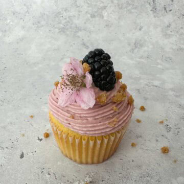 Blackberry Crumble Cupcake with Blackberry Cream Cheese Frosting and garnished with a whole blackberry and blackberry flower.