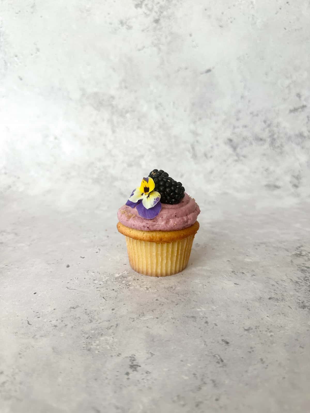 Blackberry Crumble Cupcake with Blackberry Cream Cheese Frosting and garnished with a whole blackberry and pansy flower.