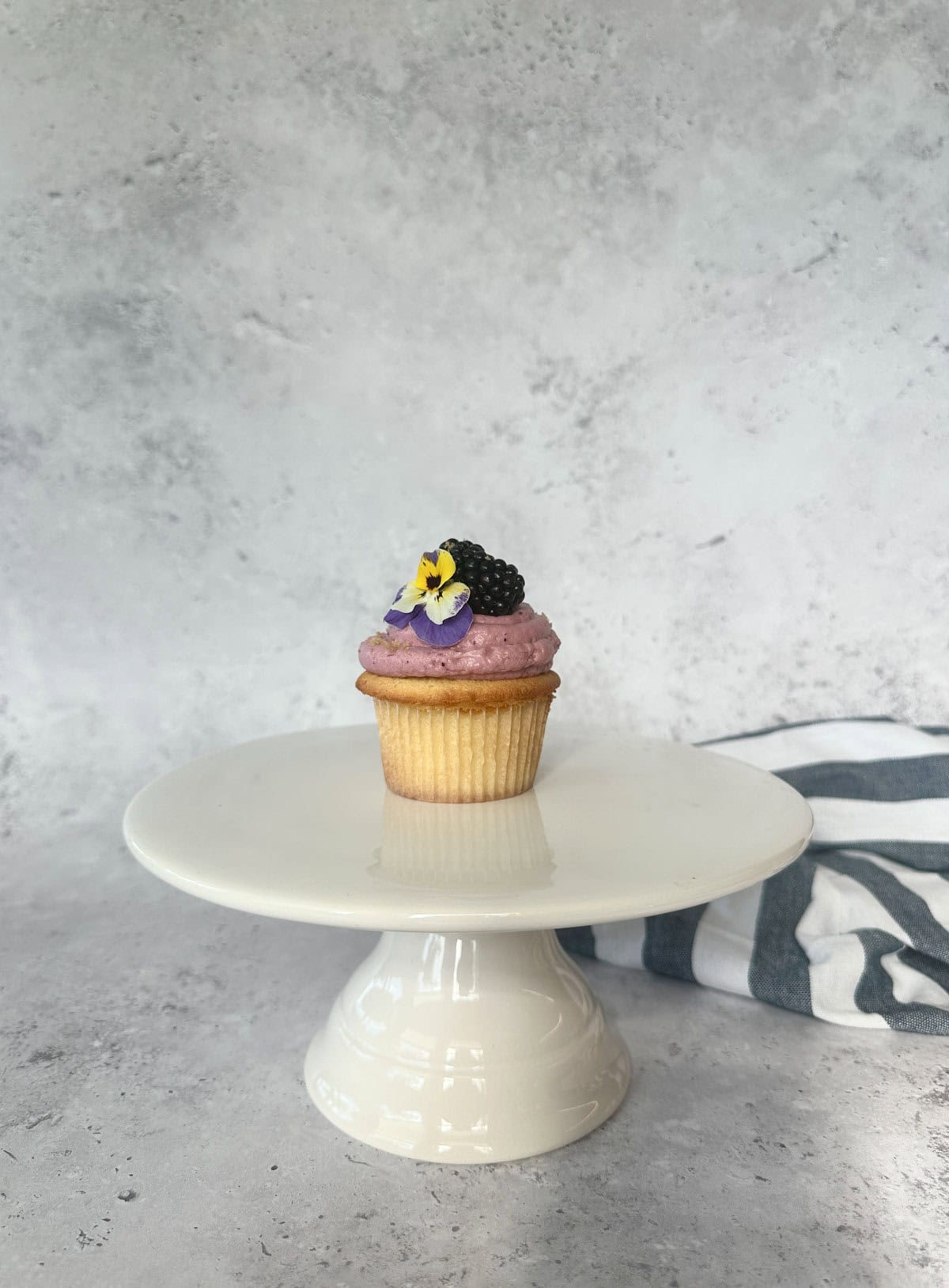 Blackberry Crumble Cupcake with Blackberry Cream Cheese Frosting and garnished with a whole blackberry and pansy flower.